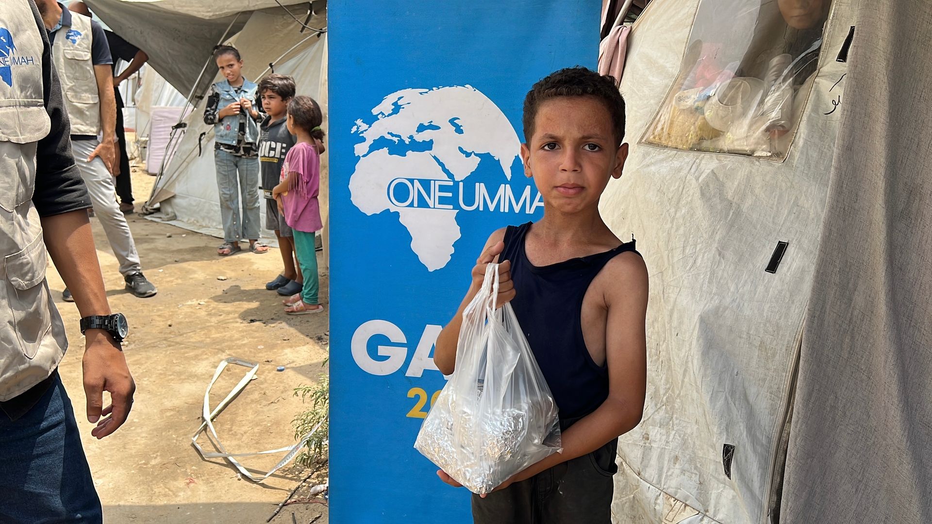 Gaza emergency aid pack on an older man’s back with destruction in the background.