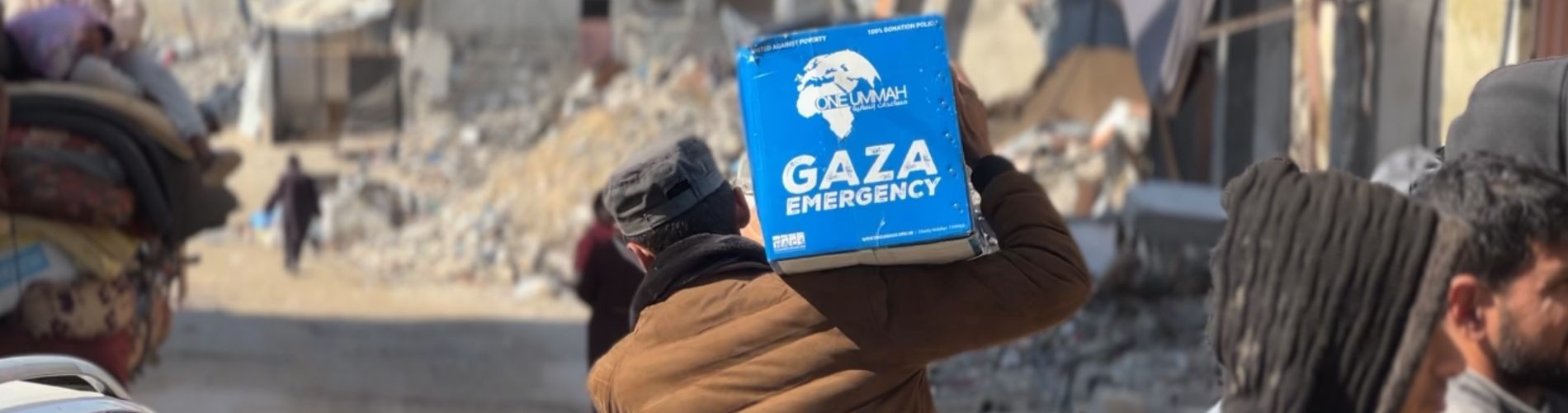 Gaza emergency aid pack on an older man’s back with destruction in the background.