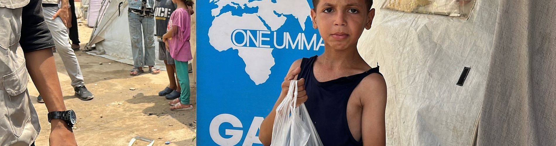 Gaza emergency aid pack on an older man’s back with destruction in the background.